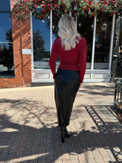 Woman wearing burgundy long sleeve top with twist front and gold detail.