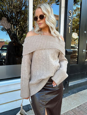 Woman wearing oversized, off the shoulder, tan sweater with brown leather skirt.