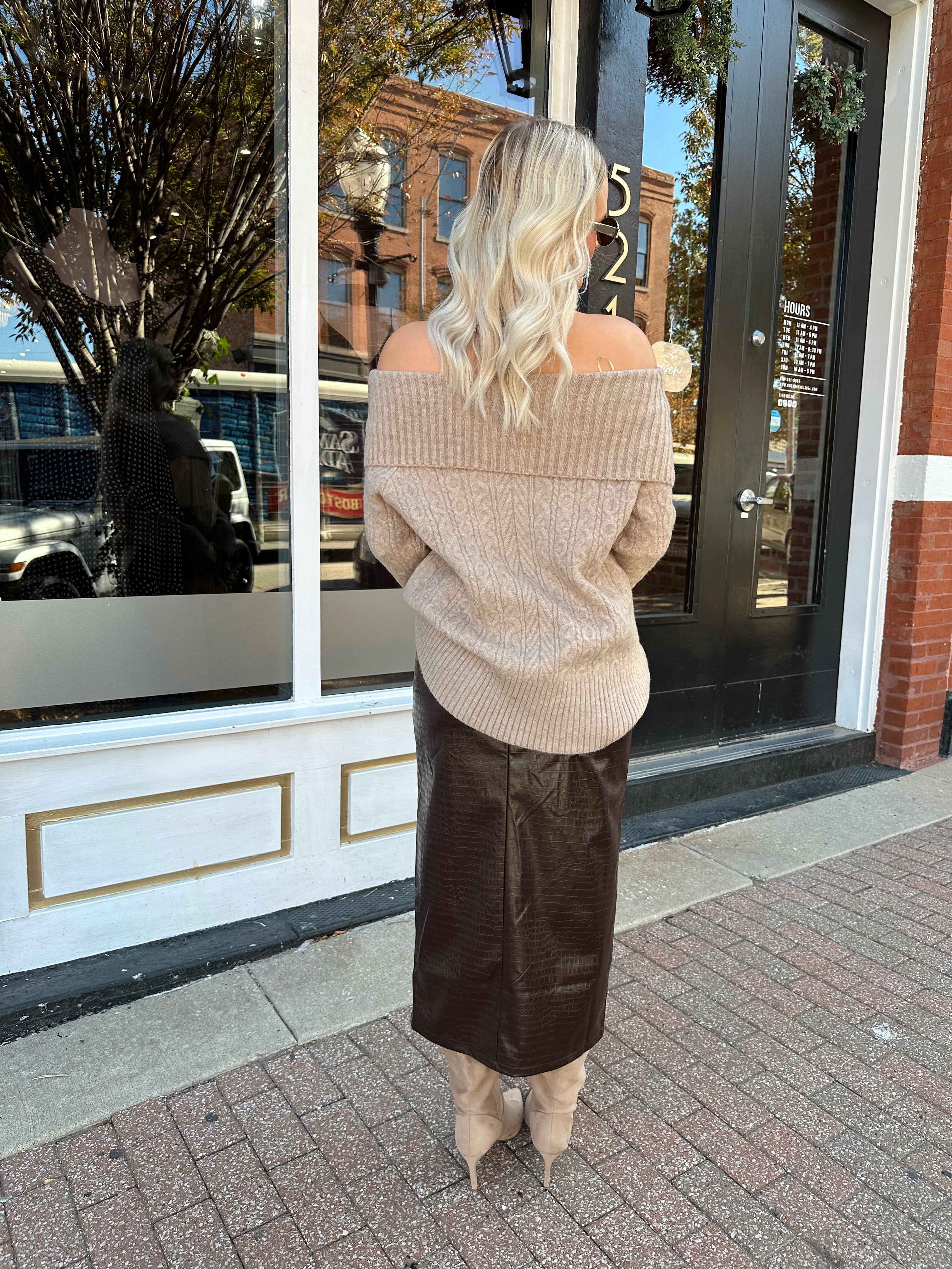 Woman wearing oversized, off the shoulder, tan sweater with brown leather skirt.
