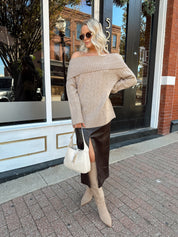 Woman wearing oversized, off the shoulder, tan sweater with brown leather skirt.