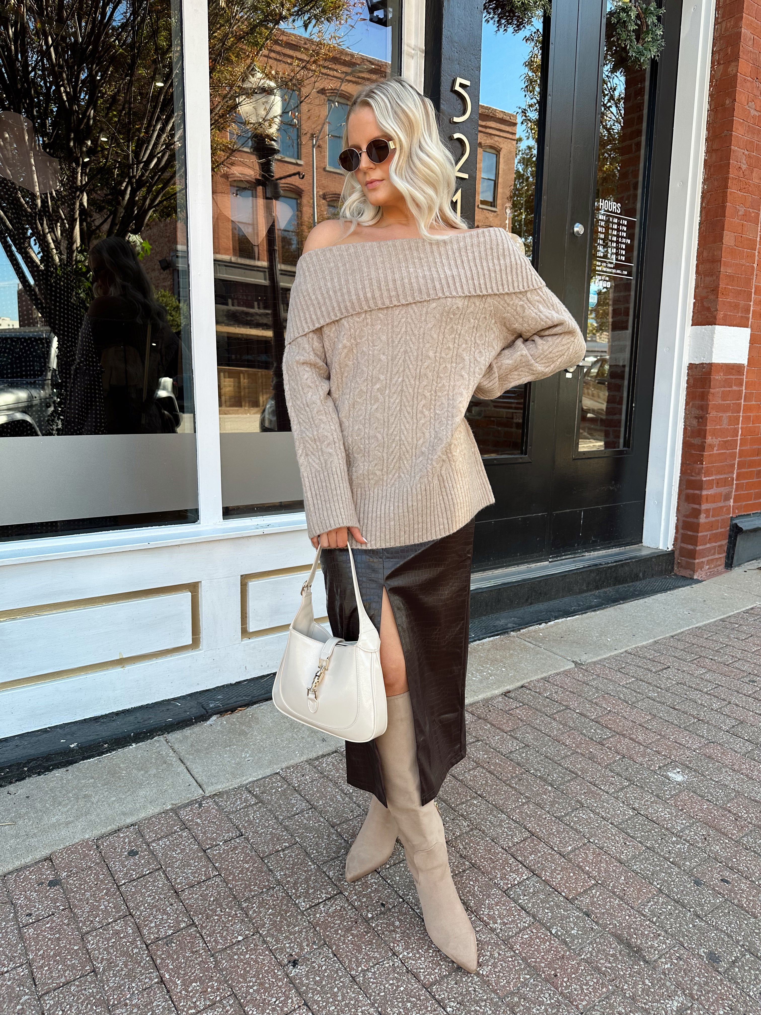 Woman wearing oversized, off the shoulder, tan sweater with brown leather skirt.
