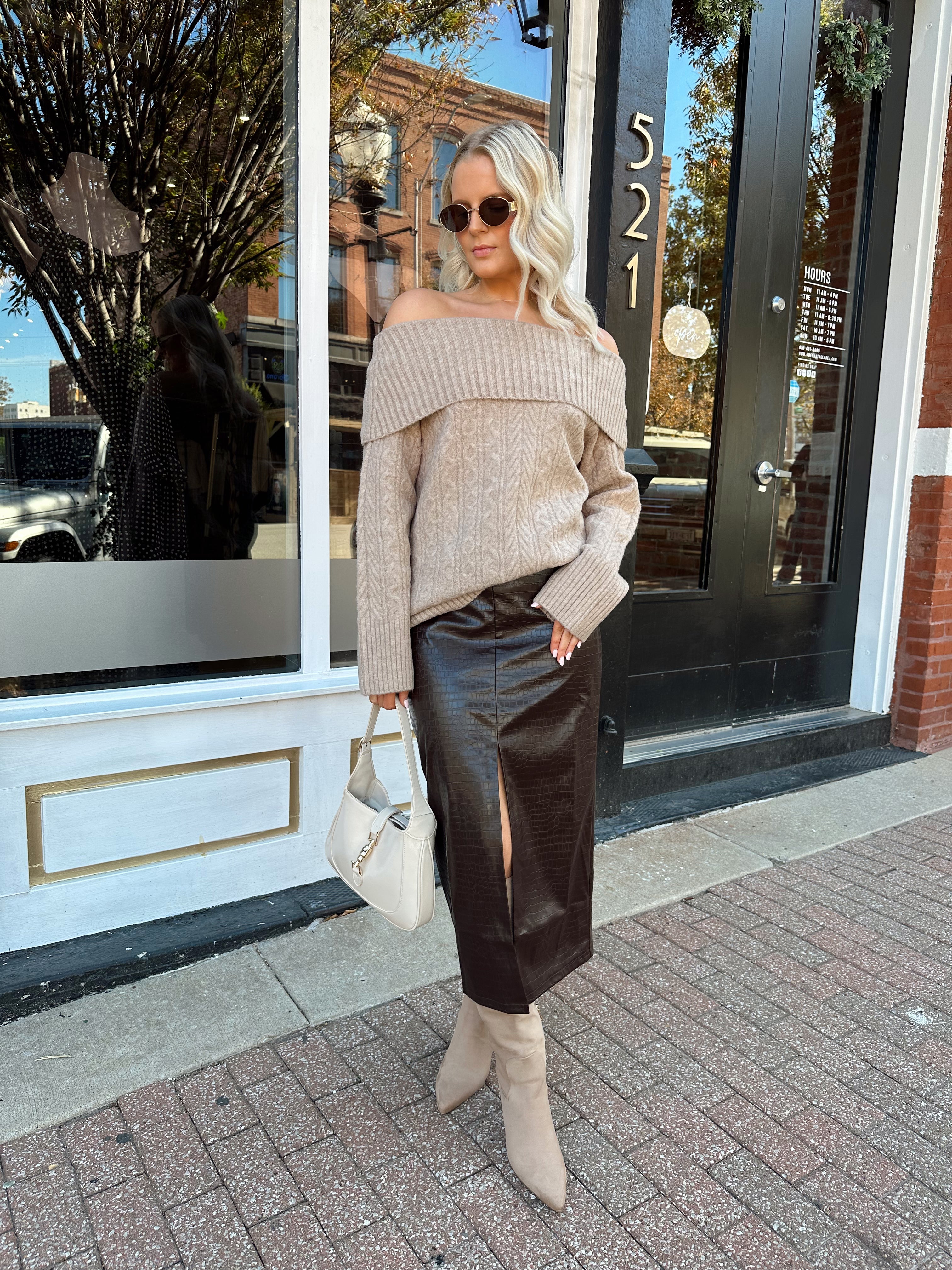 Woman wearing oversized, off the shoulder, tan sweater with brown leather skirt.