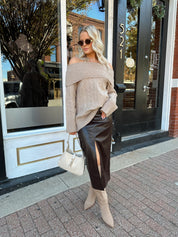 Woman wearing oversized, off the shoulder, tan sweater with brown leather skirt.