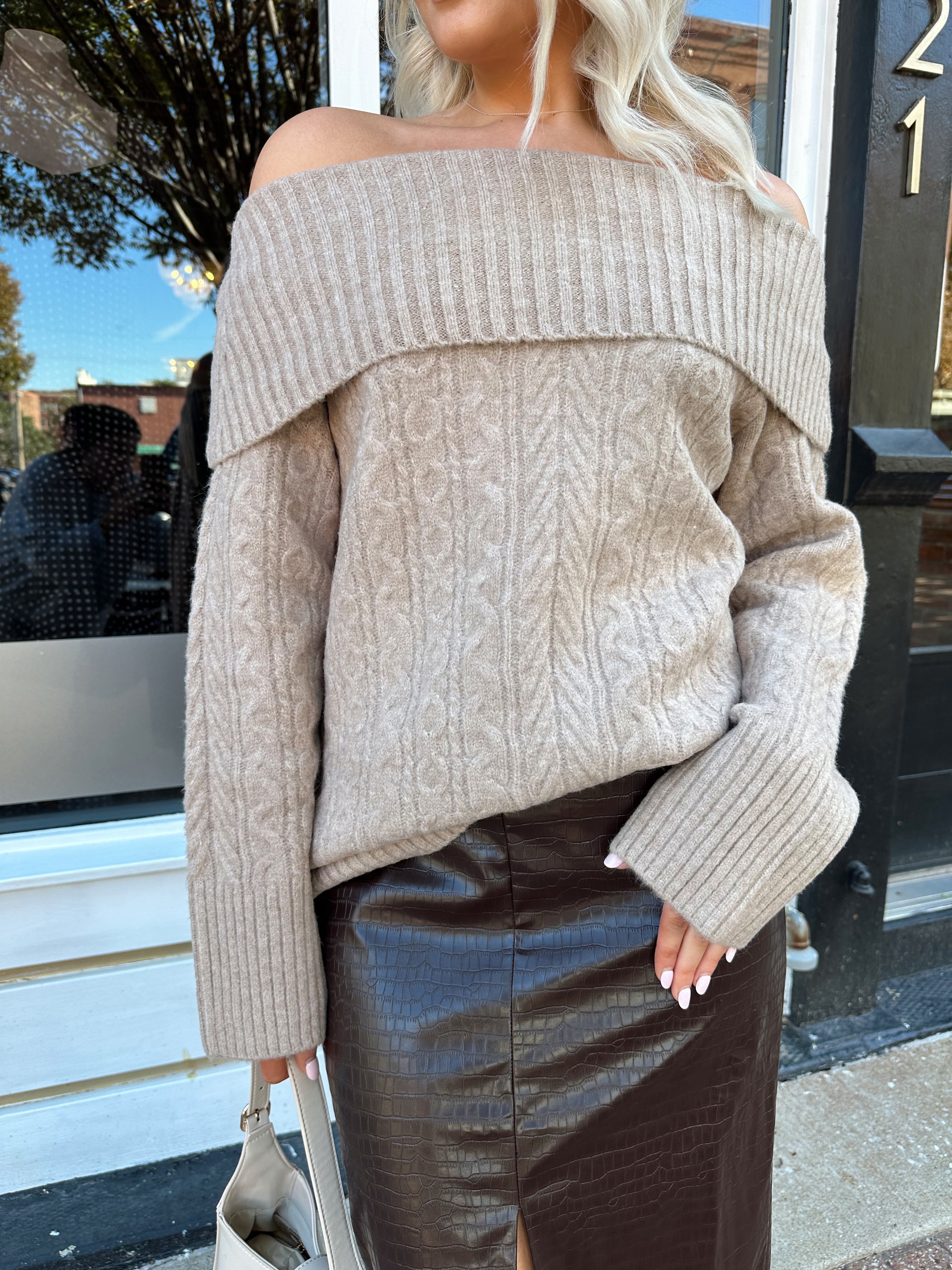 Woman wearing oversized, off the shoulder, tan sweater with brown leather skirt.