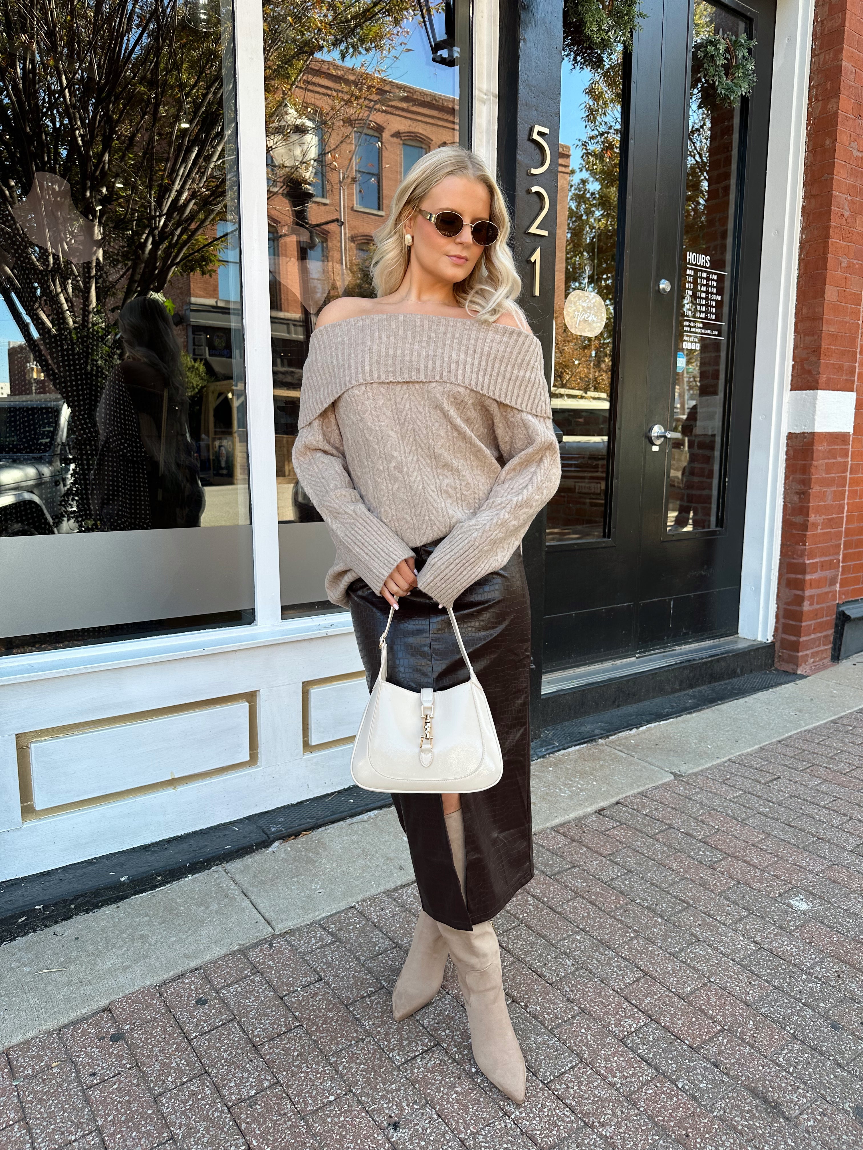 Woman wearing oversized, off the shoulder, tan sweater with brown leather skirt.