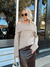 Woman wearing oversized, off the shoulder, tan sweater with brown leather skirt.