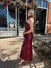 Woman wearing plum satin maxi dress with halter neckline.