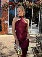 Woman wearing plum satin maxi dress with halter neckline.