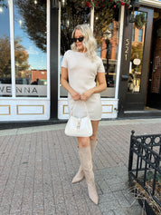 Woman wearing oatmeal knit short sleeve sweater dress and black trench coat.