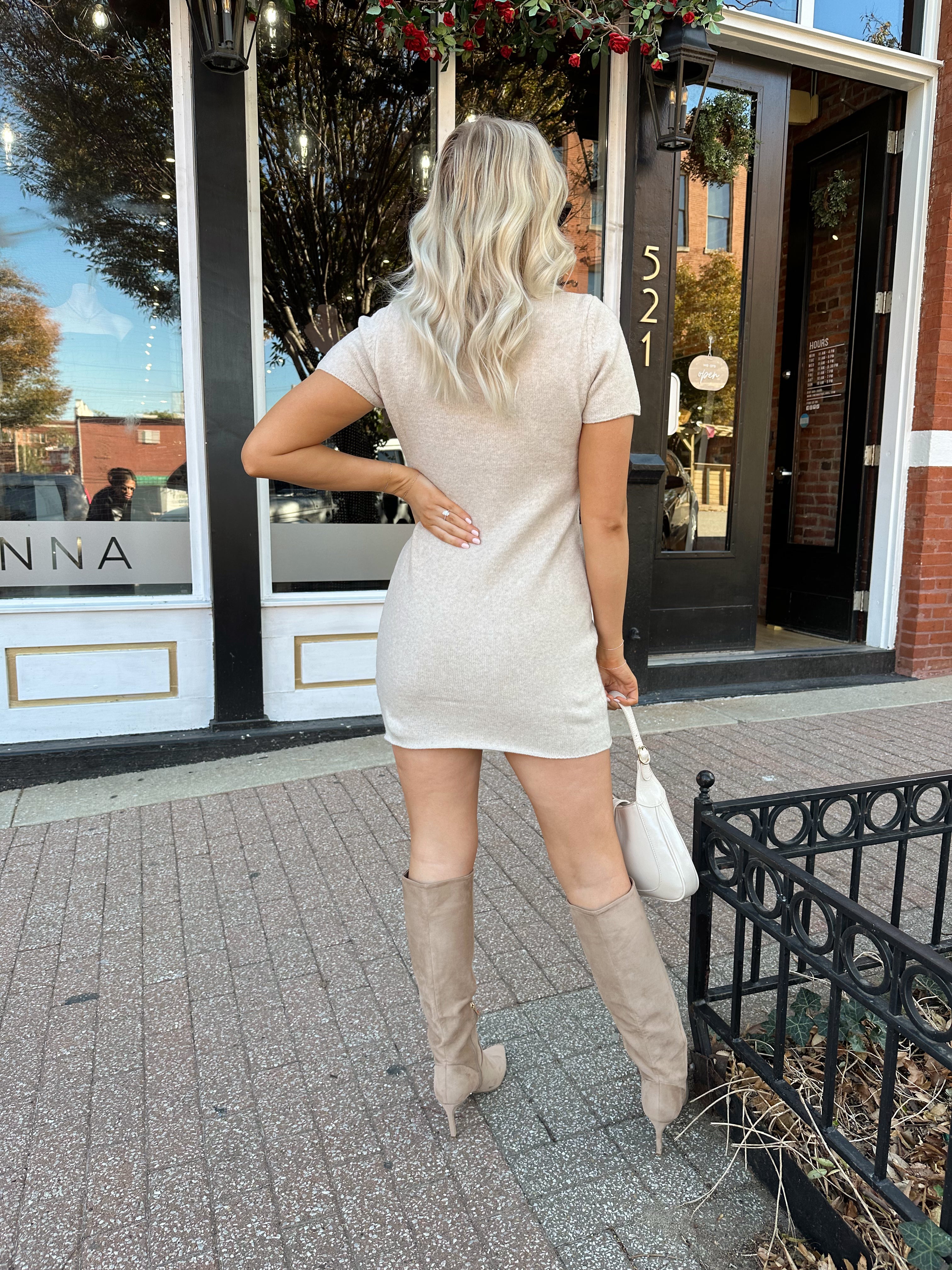 Woman wearing oatmeal knit short sleeve sweater dress and black trench coat.