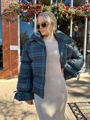 Woman wearing navy plaid puffer coat with oversized fit and draw string cuffs.