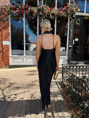 Woman wearing black satin maxi dress with halter neckline.