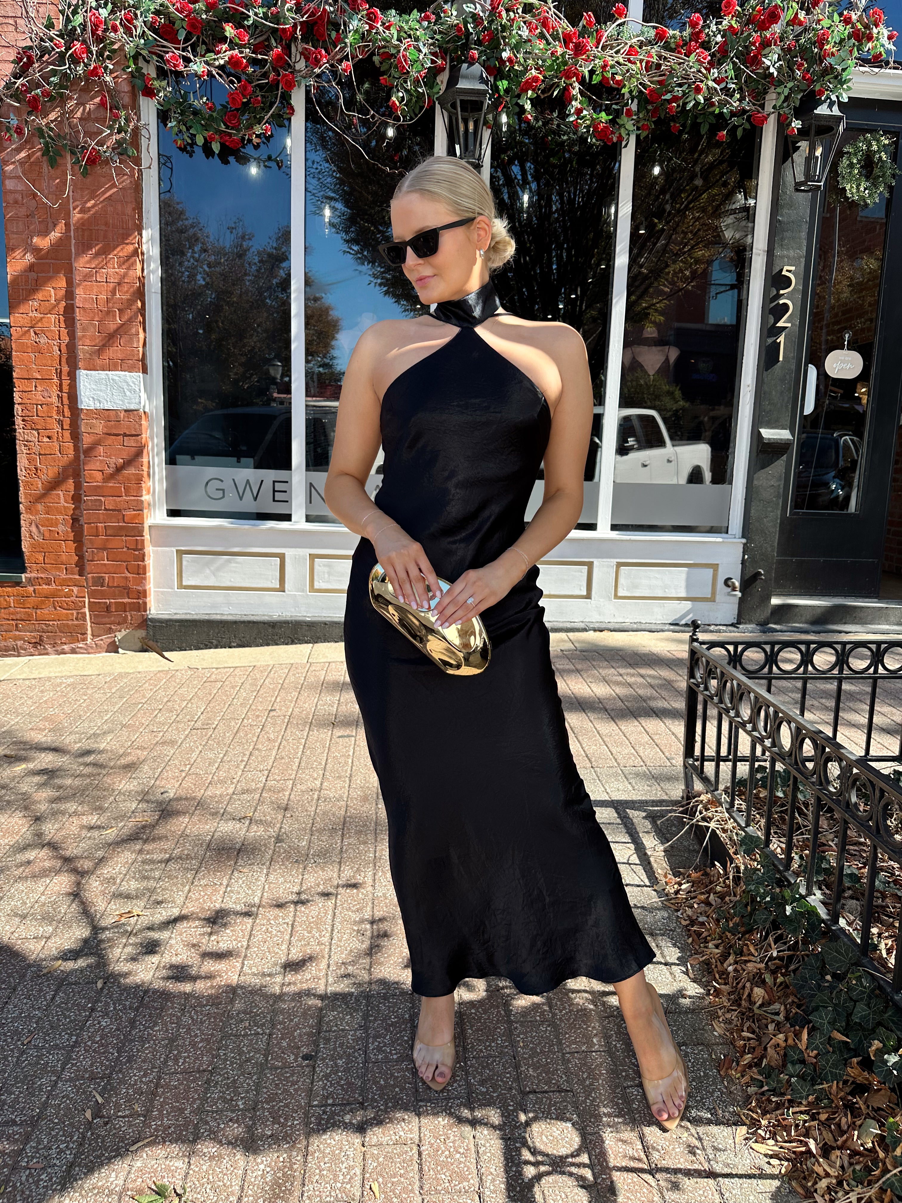 Woman wearing black satin maxi dress with halter neckline.