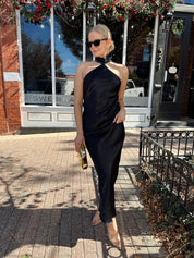 Woman wearing black satin maxi dress with halter neckline.