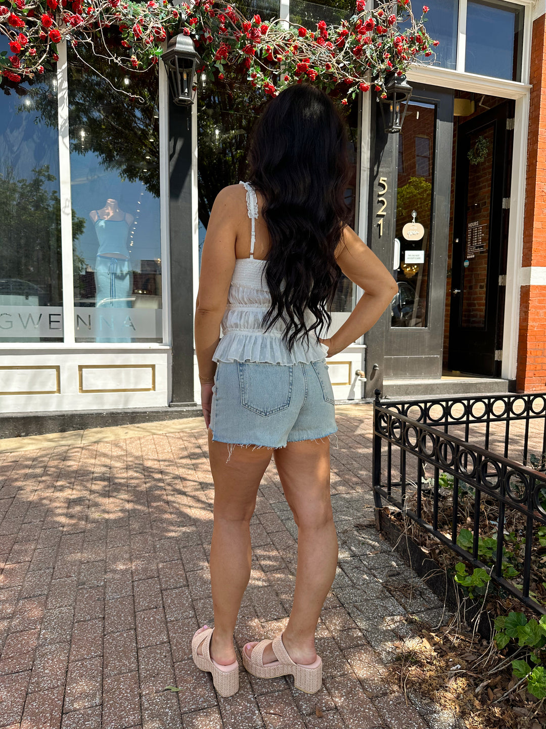 Woman wearing light wash, high waisted denim short with raw hem.