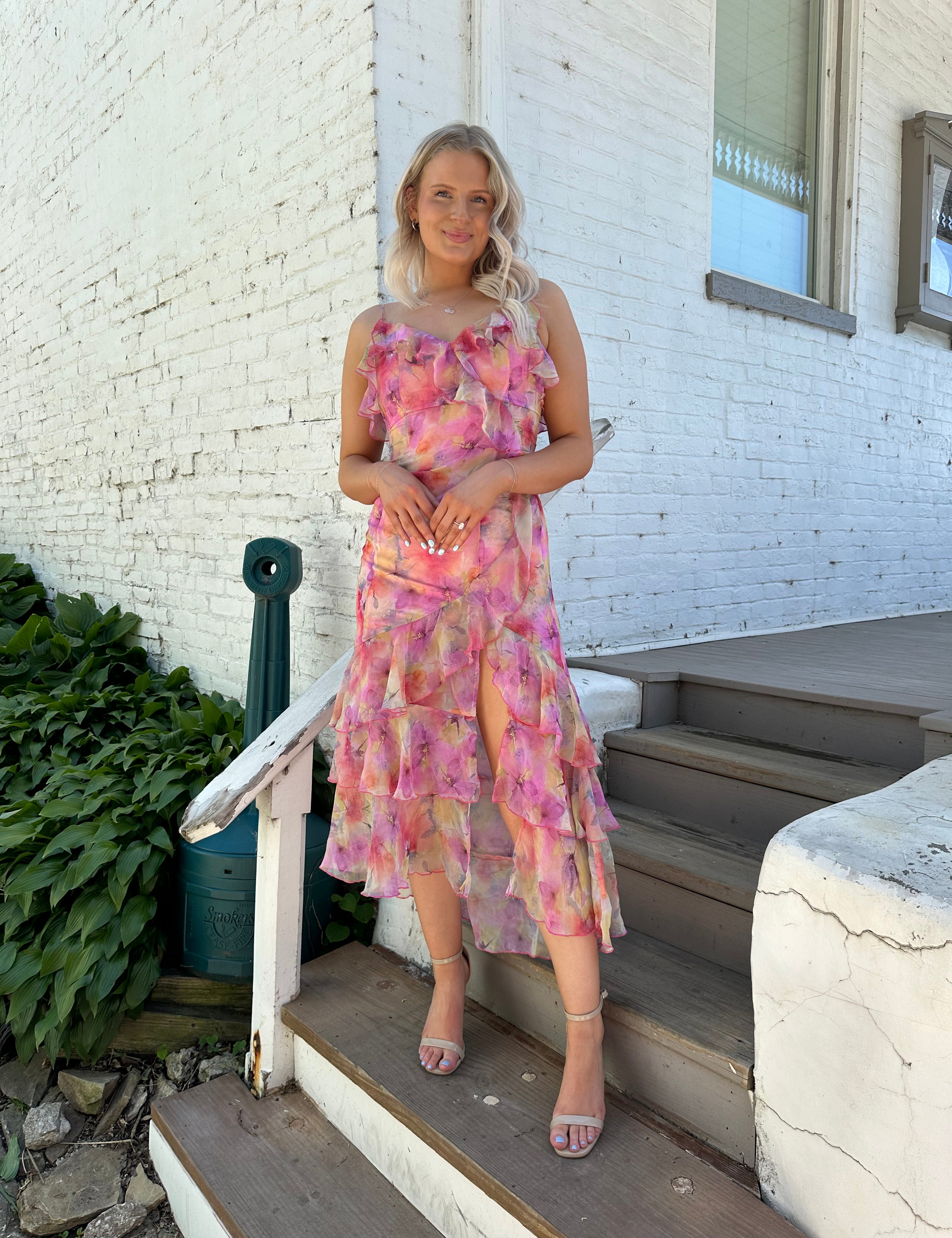 Woman wearing a pink and yellow floral tiered midi dress with ruffles and a front slit
