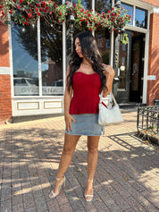 Woman wearing red strapless peplum top with denim mini skirt. 