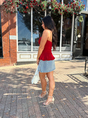 Woman wearing red strapless peplum top with denim mini skirt. 