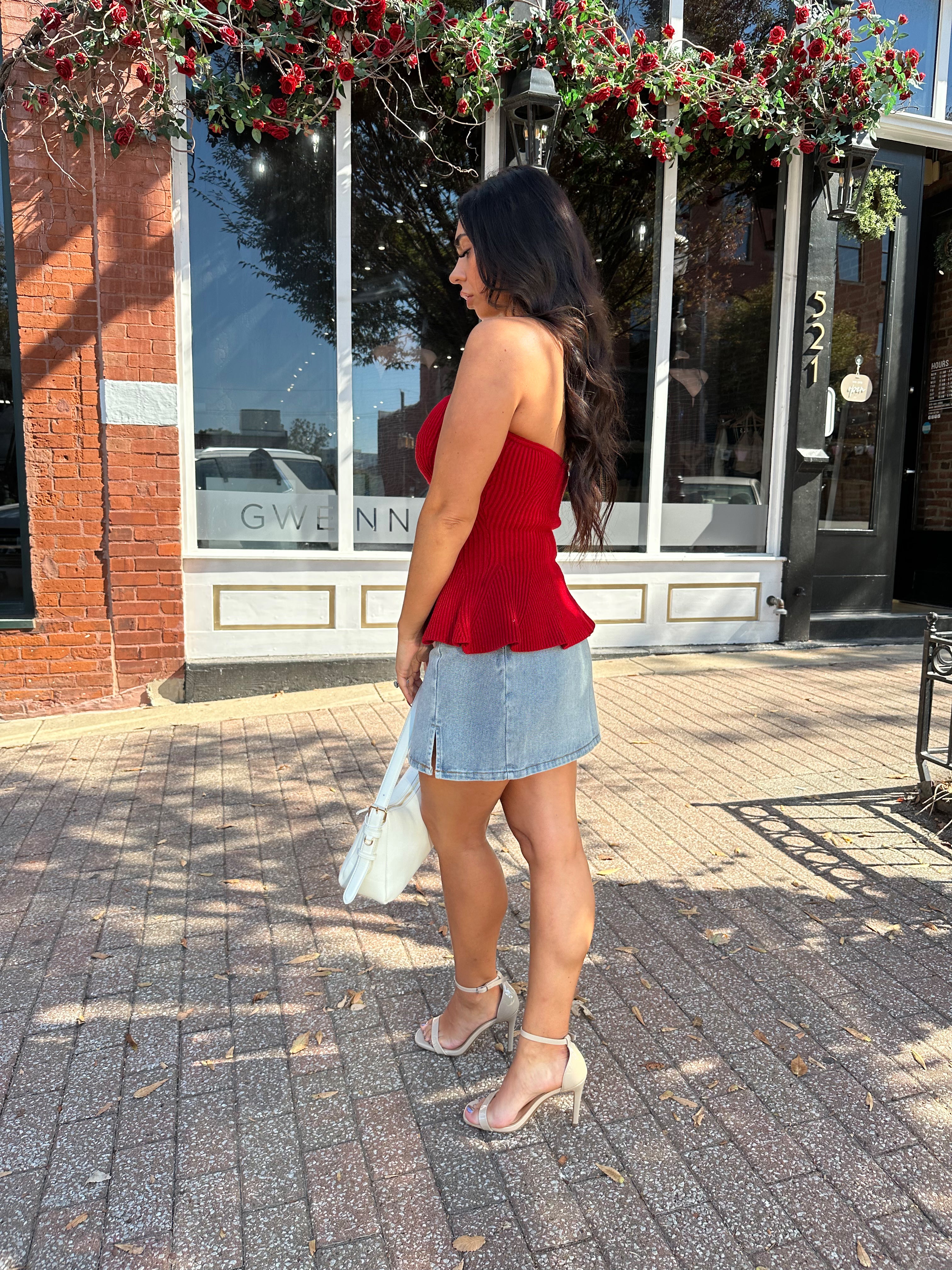 Woman wearing red strapless peplum top with denim mini skirt. 