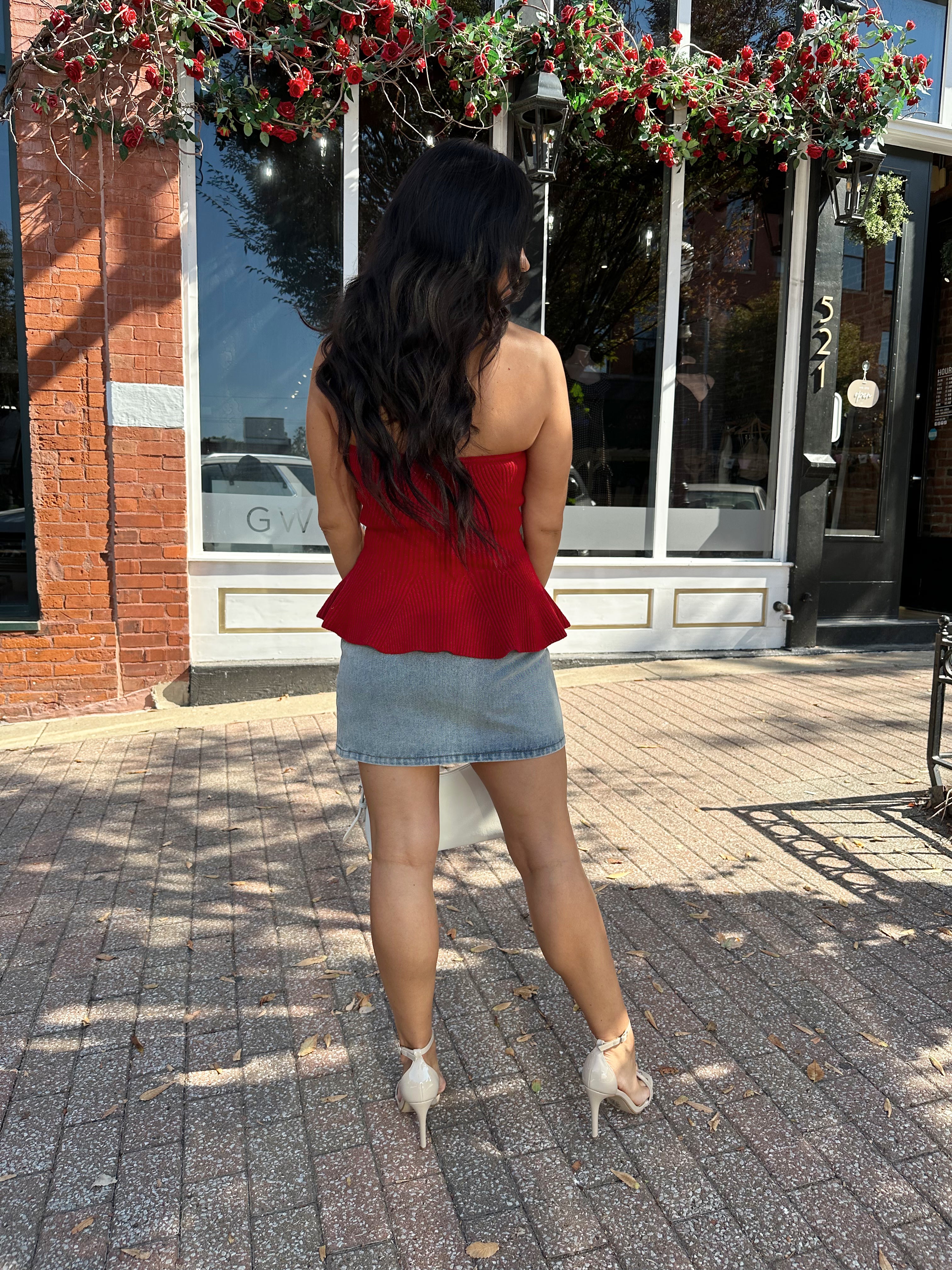 Woman wearing red strapless peplum top with denim mini skirt. 