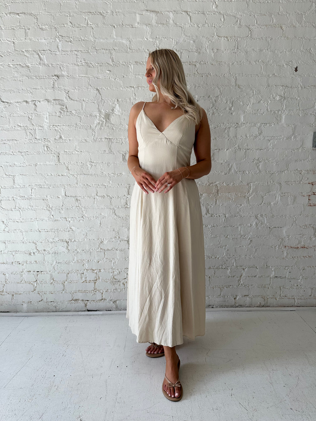 Woman wearing beige linen midi dress with an open tie back, and functional pockets.