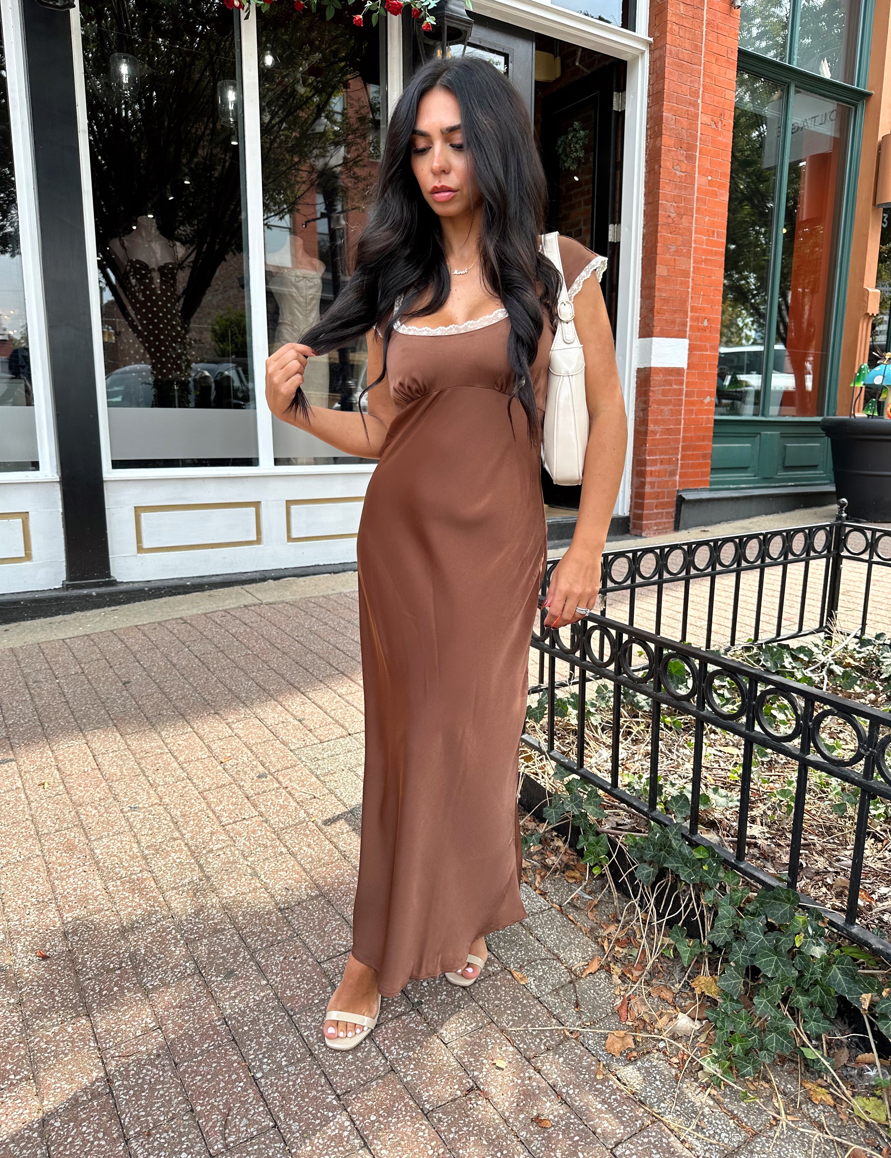Woman wearing copper brown satin midi dress with white ruffle trim and tie back. 
