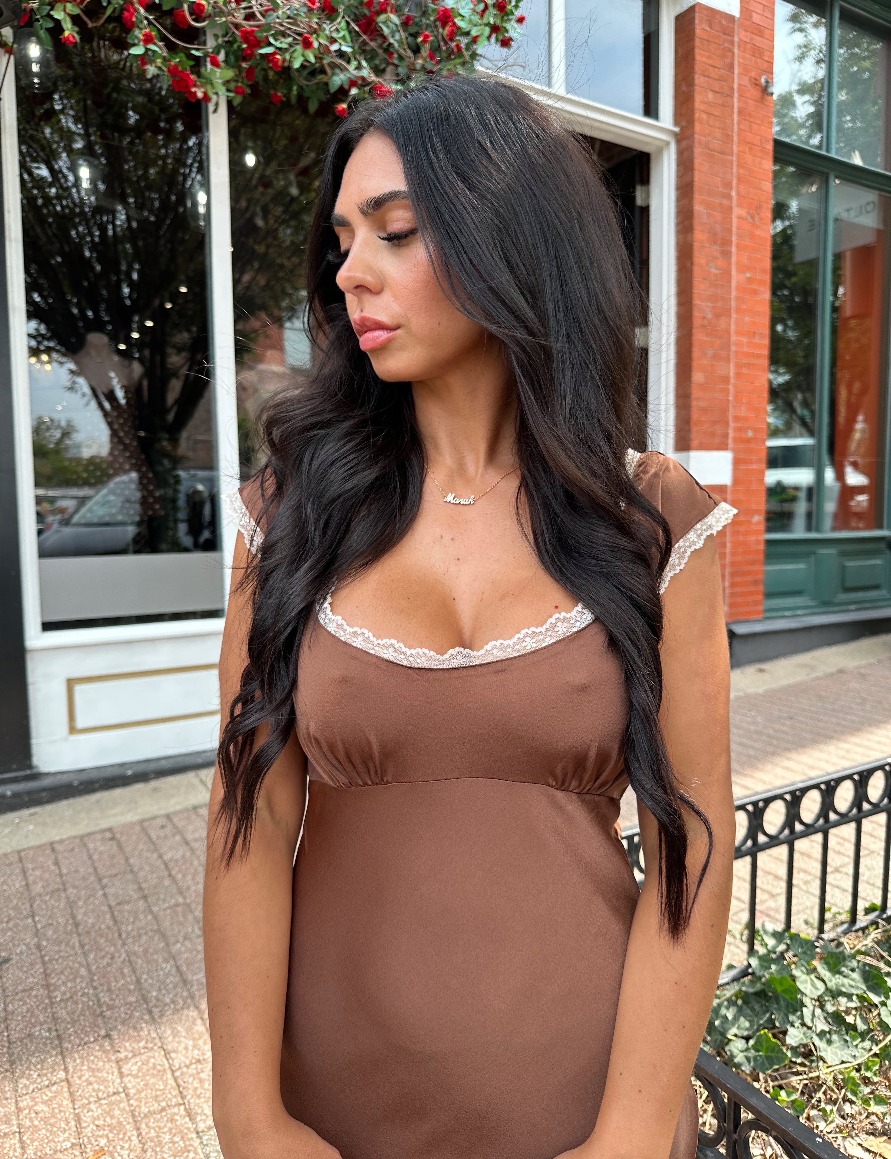 Woman wearing copper brown satin midi dress with white ruffle trim and tie back. 