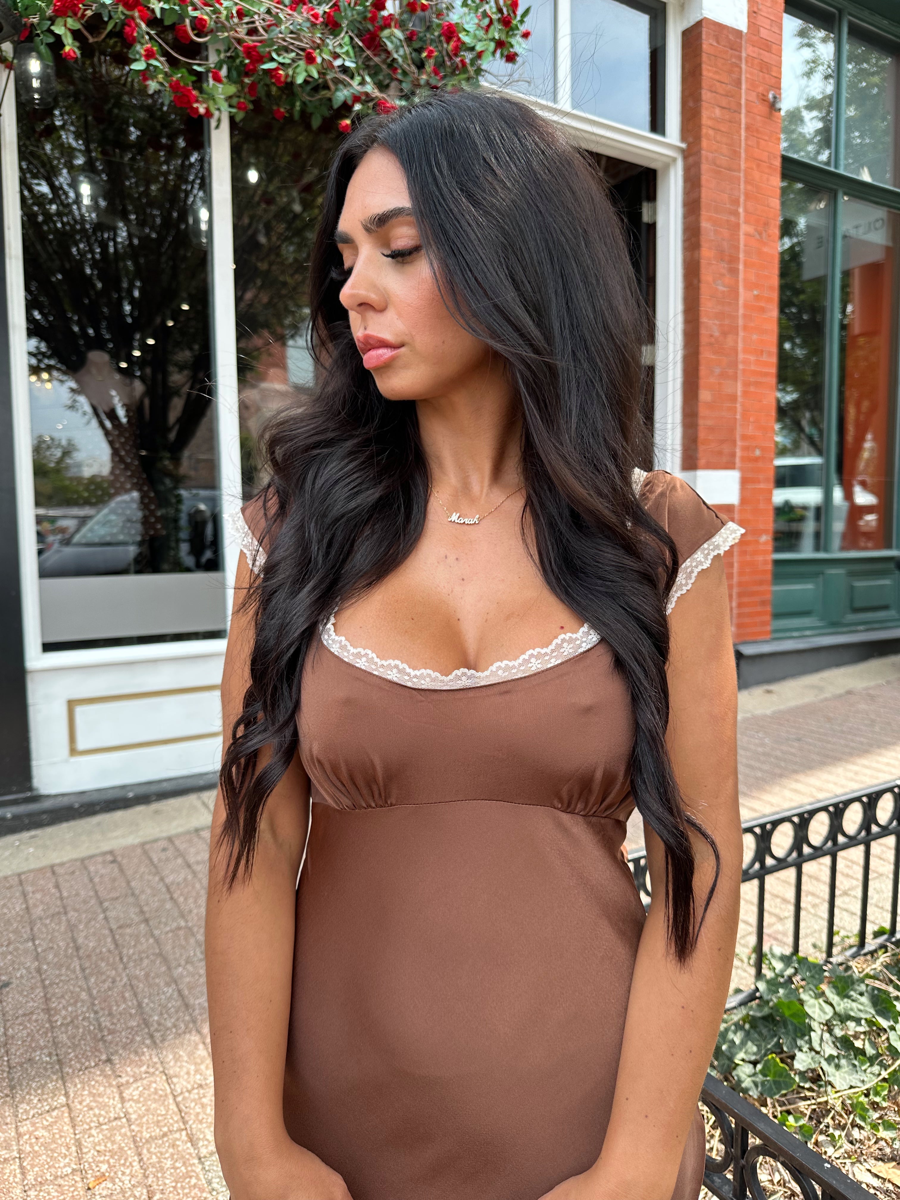 Woman wearing copper brown satin midi dress with white ruffle trim and tie back. 
