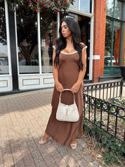 Woman wearing copper brown satin midi dress with white ruffle trim and tie back. 