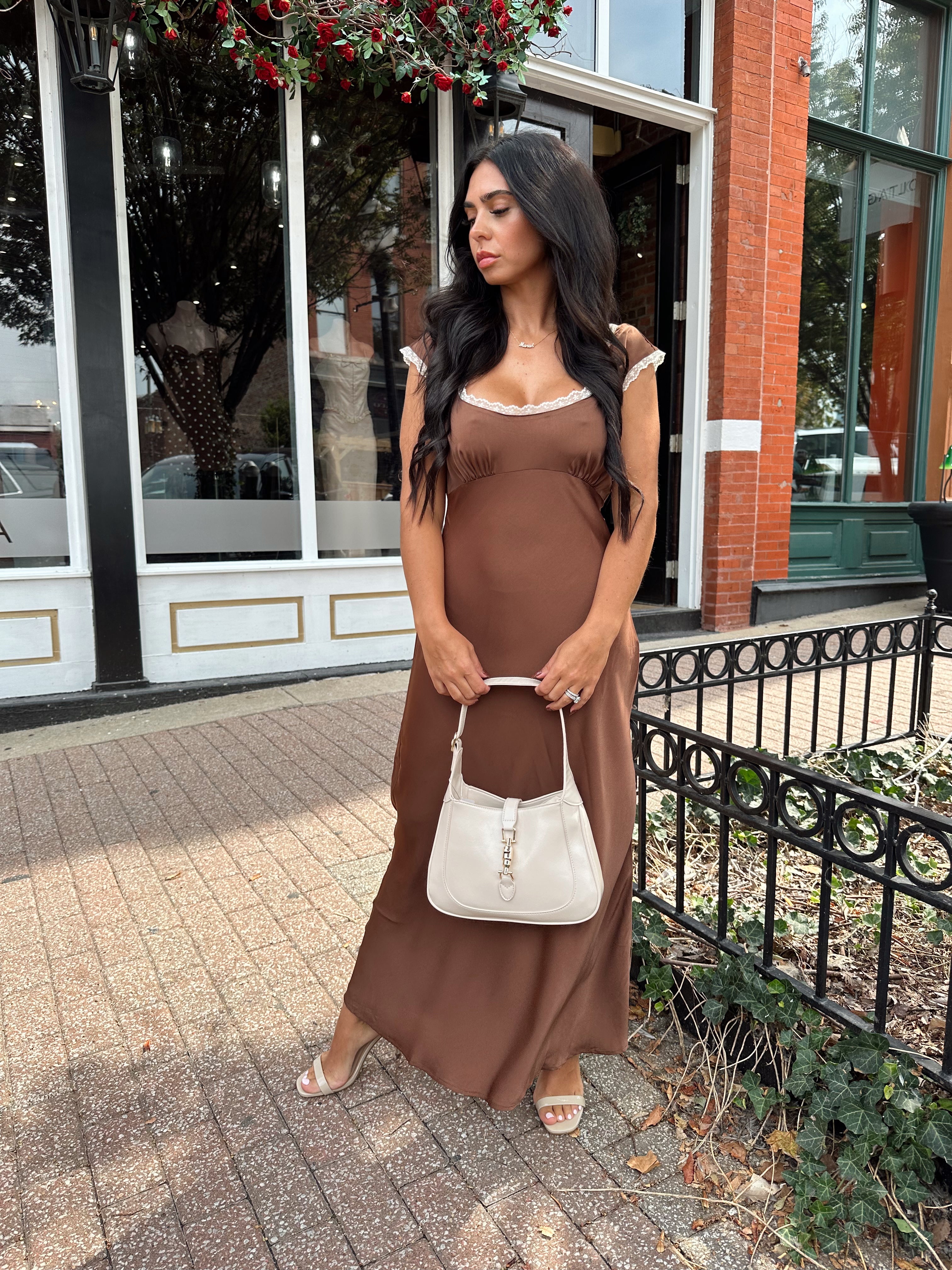Woman wearing copper brown satin midi dress with white ruffle trim and tie back. 