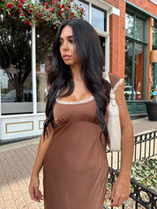 Woman wearing copper brown satin midi dress with white ruffle trim and tie back. 
