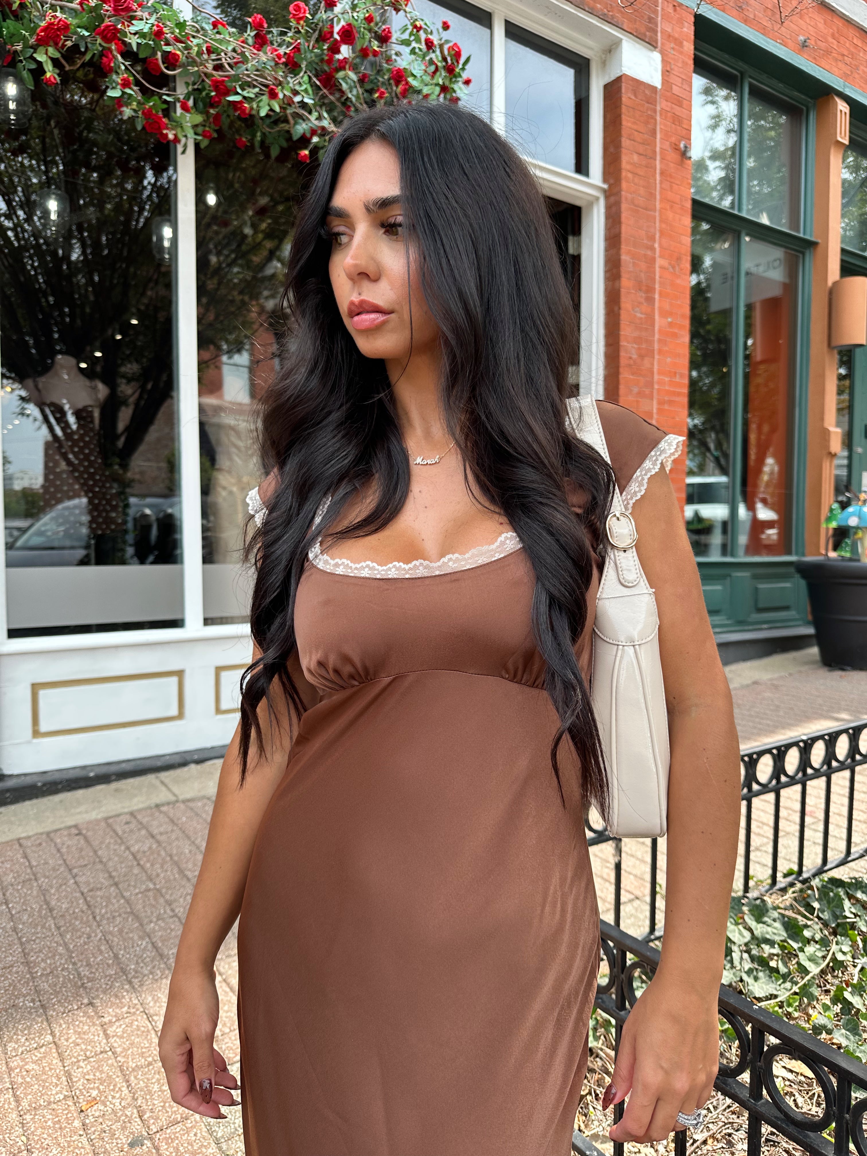 Woman wearing copper brown satin midi dress with white ruffle trim and tie back. 