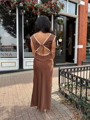 Woman wearing copper brown satin midi dress with white ruffle trim and tie back. 