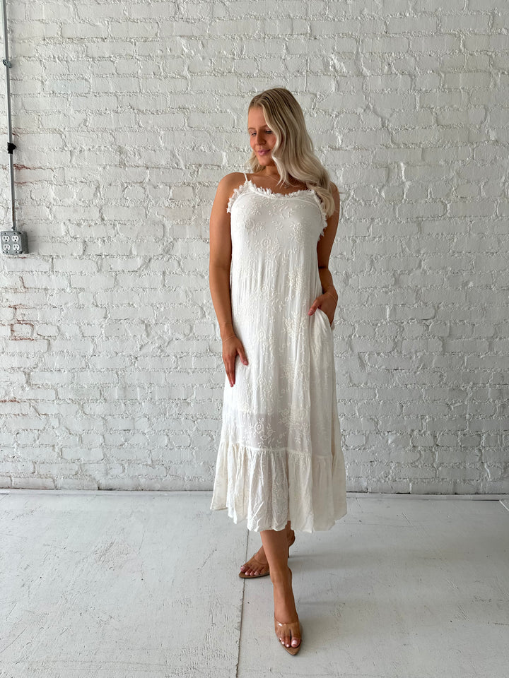 Woman wearing cream embroidered midi dress with fringe neckline.