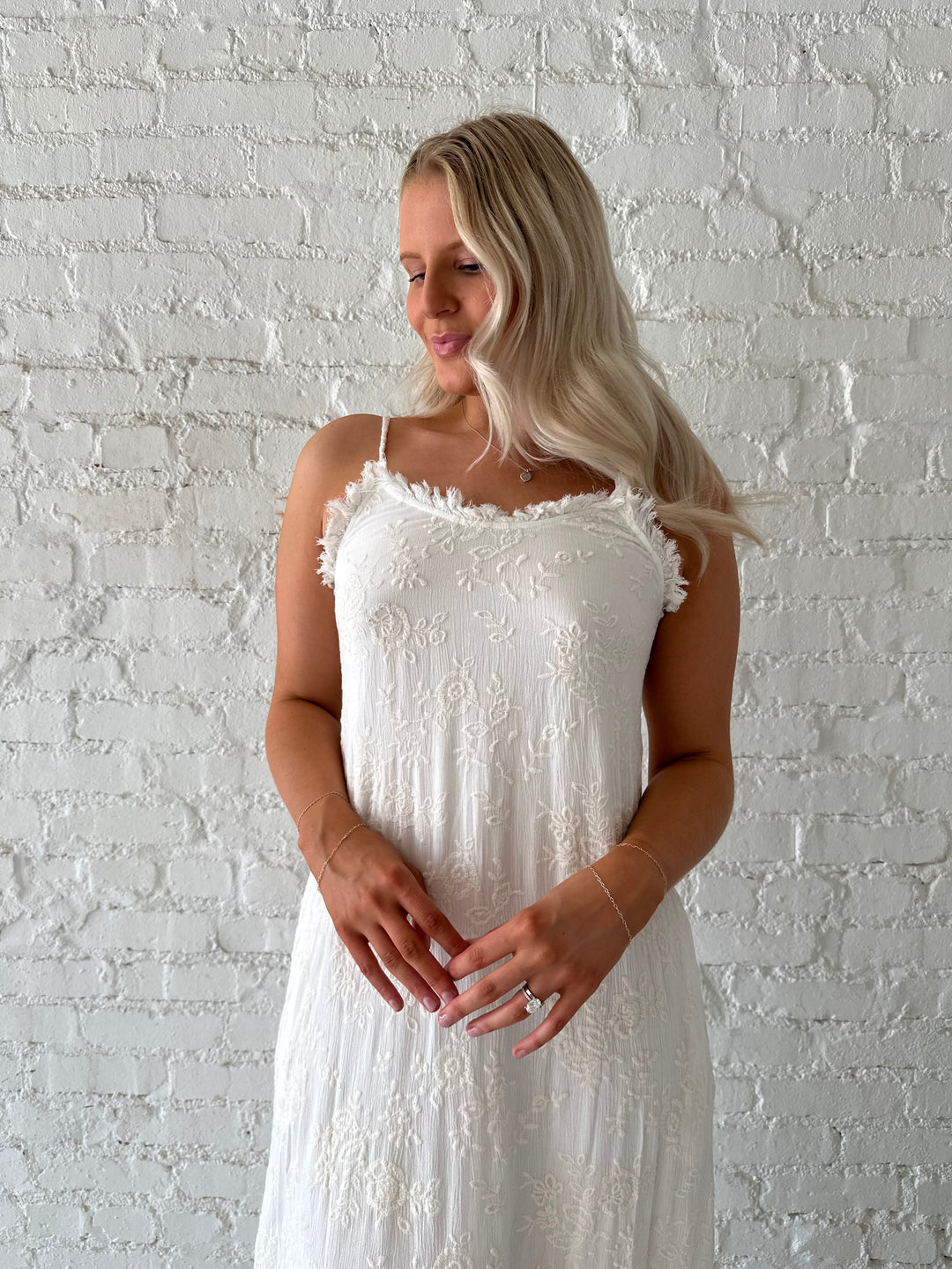 Woman wearing cream embroidered midi dress with fringe neckline.