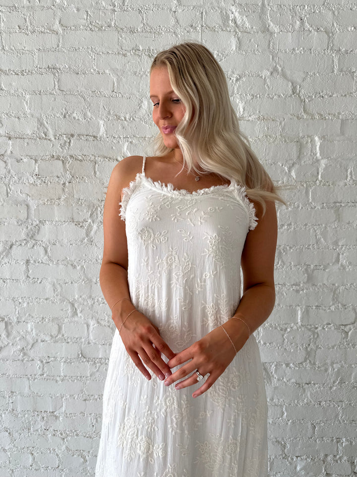 Woman wearing cream embroidered midi dress with fringe neckline.