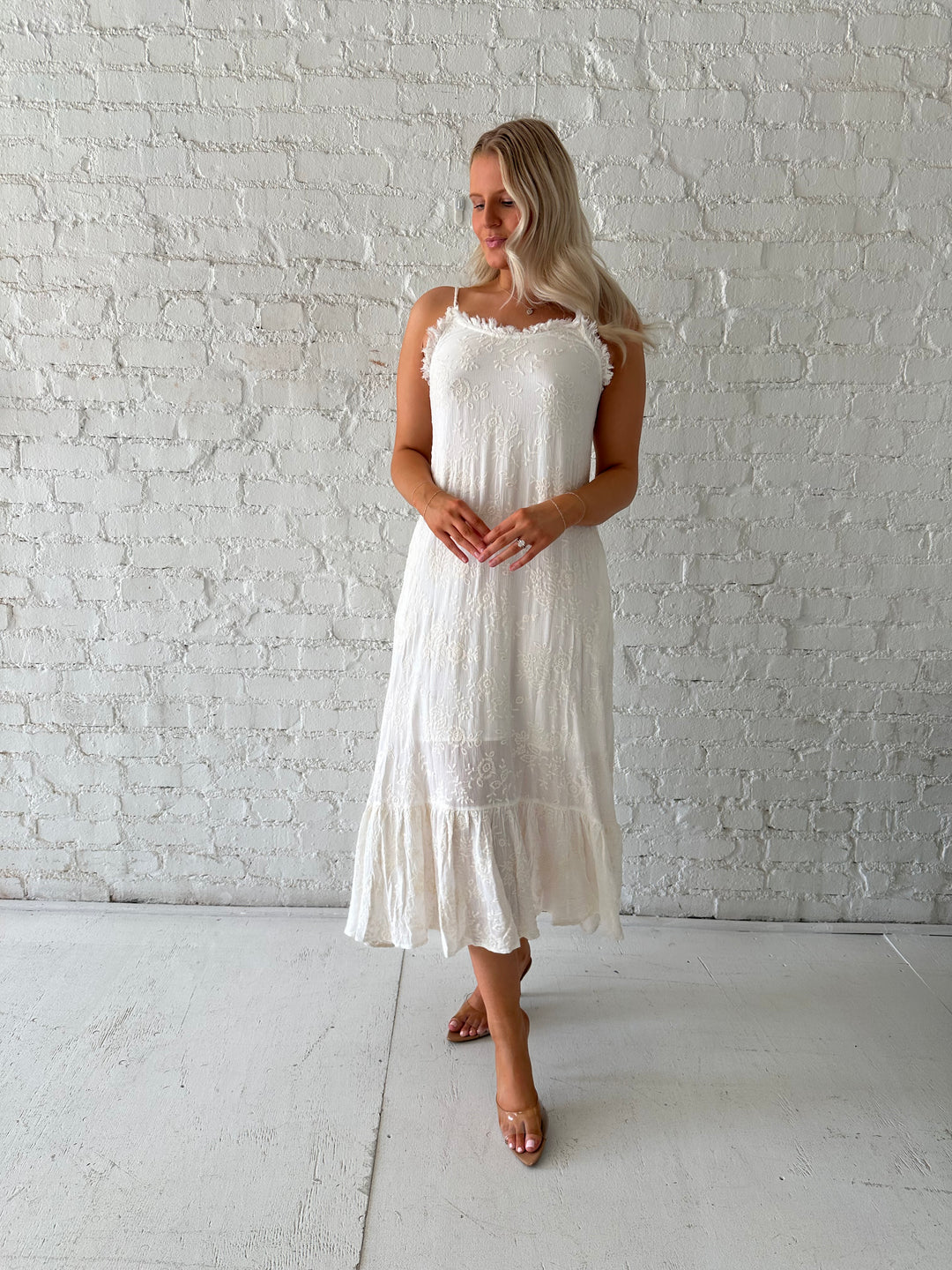 Woman wearing cream embroidered midi dress with fringe neckline.