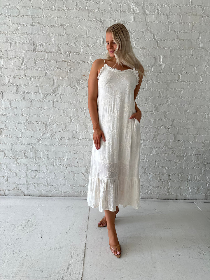 Woman wearing cream embroidered midi dress with fringe neckline.