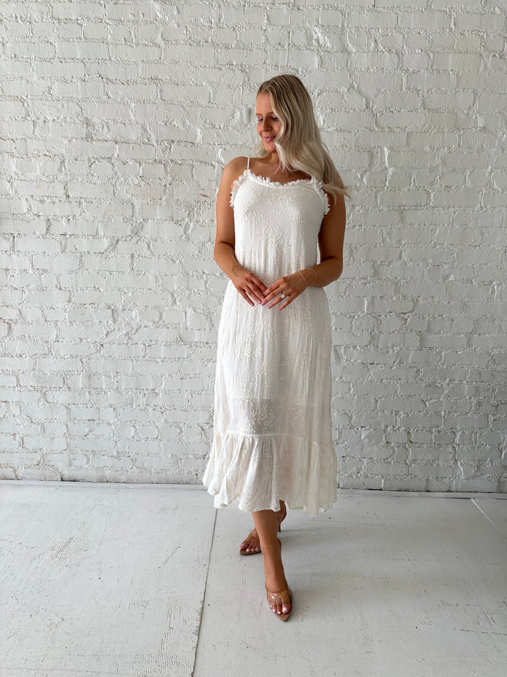 Woman wearing cream embroidered midi dress with fringe neckline.