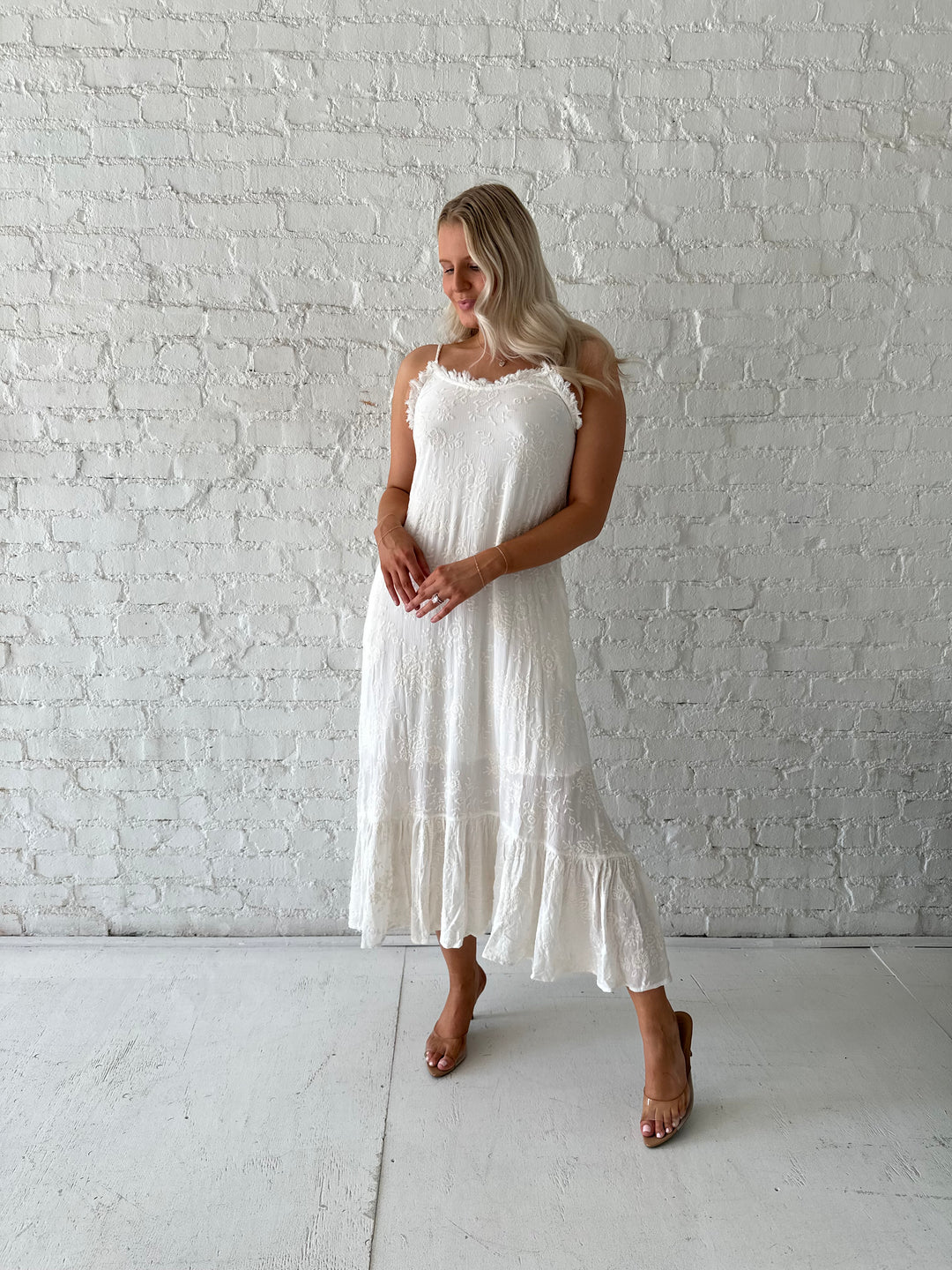 Woman wearing cream embroidered midi dress with fringe neckline.