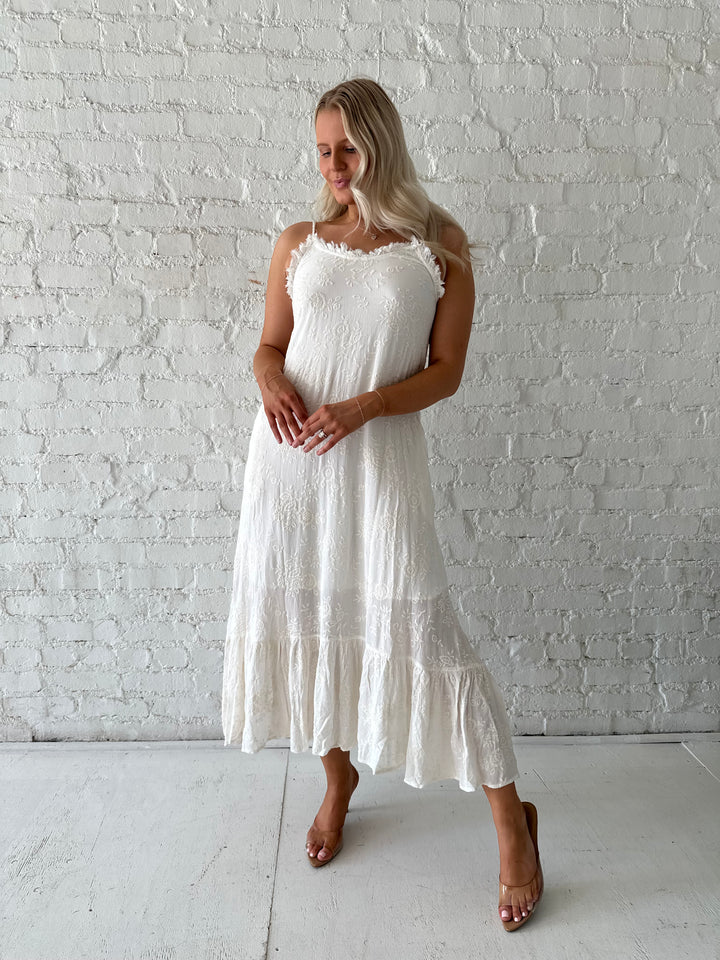 Woman wearing cream embroidered midi dress with fringe neckline.