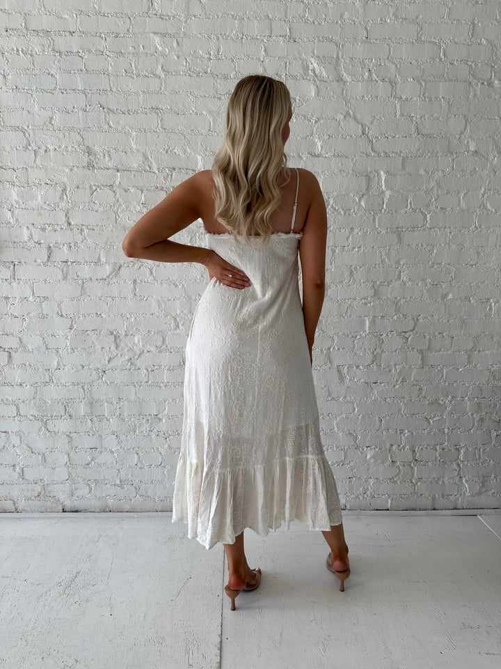 Woman wearing cream embroidered midi dress with fringe neckline.