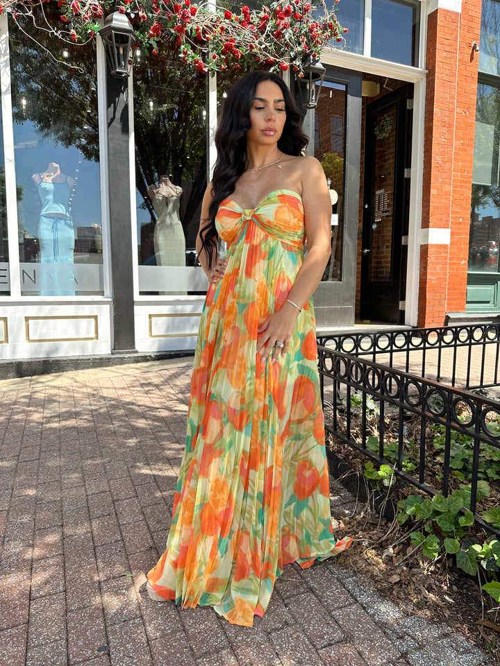 Woman wearing orange tropical plated maxi dress with sweetheart neckline, and knot detail.