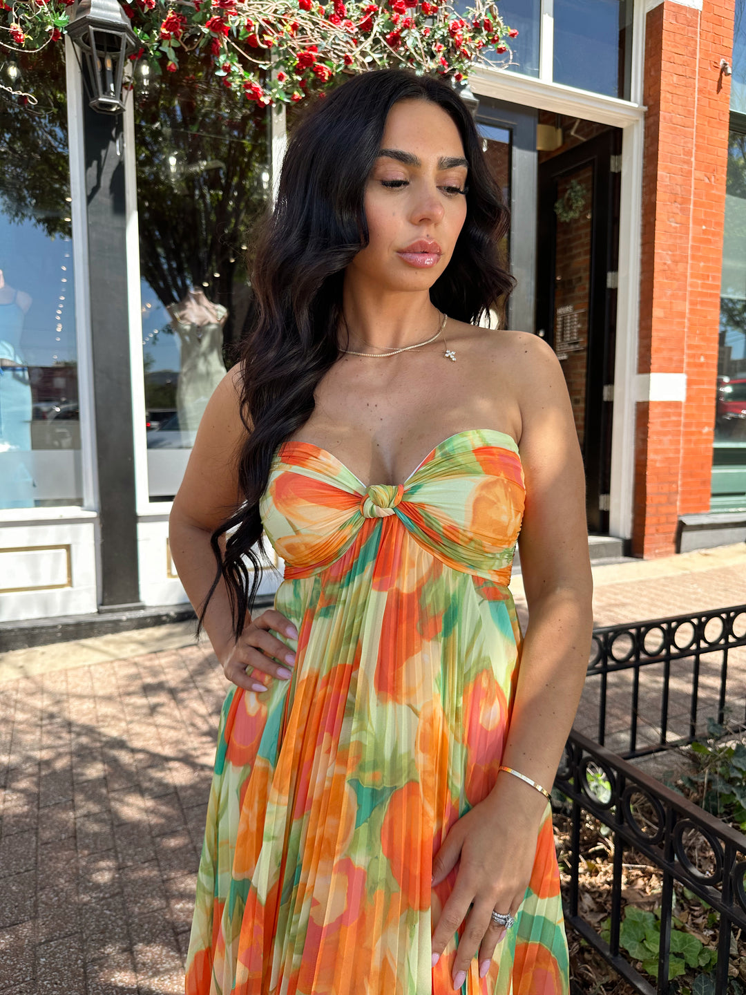 Woman wearing orange tropical plated maxi dress with sweetheart neckline, and knot detail.