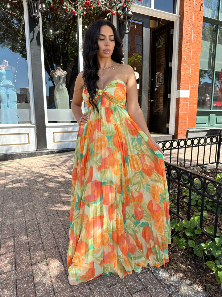 Woman wearing orange tropical plated maxi dress with sweetheart neckline, and knot detail.