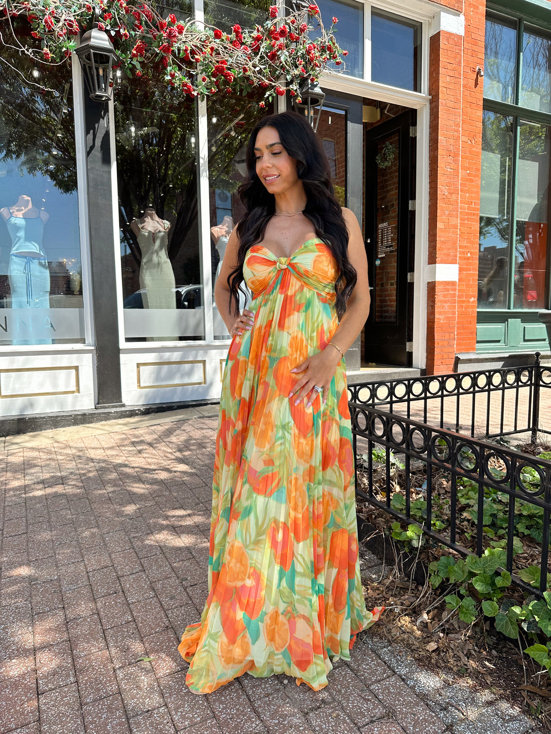 Woman wearing orange tropical plated maxi dress with sweetheart neckline, and knot detail.