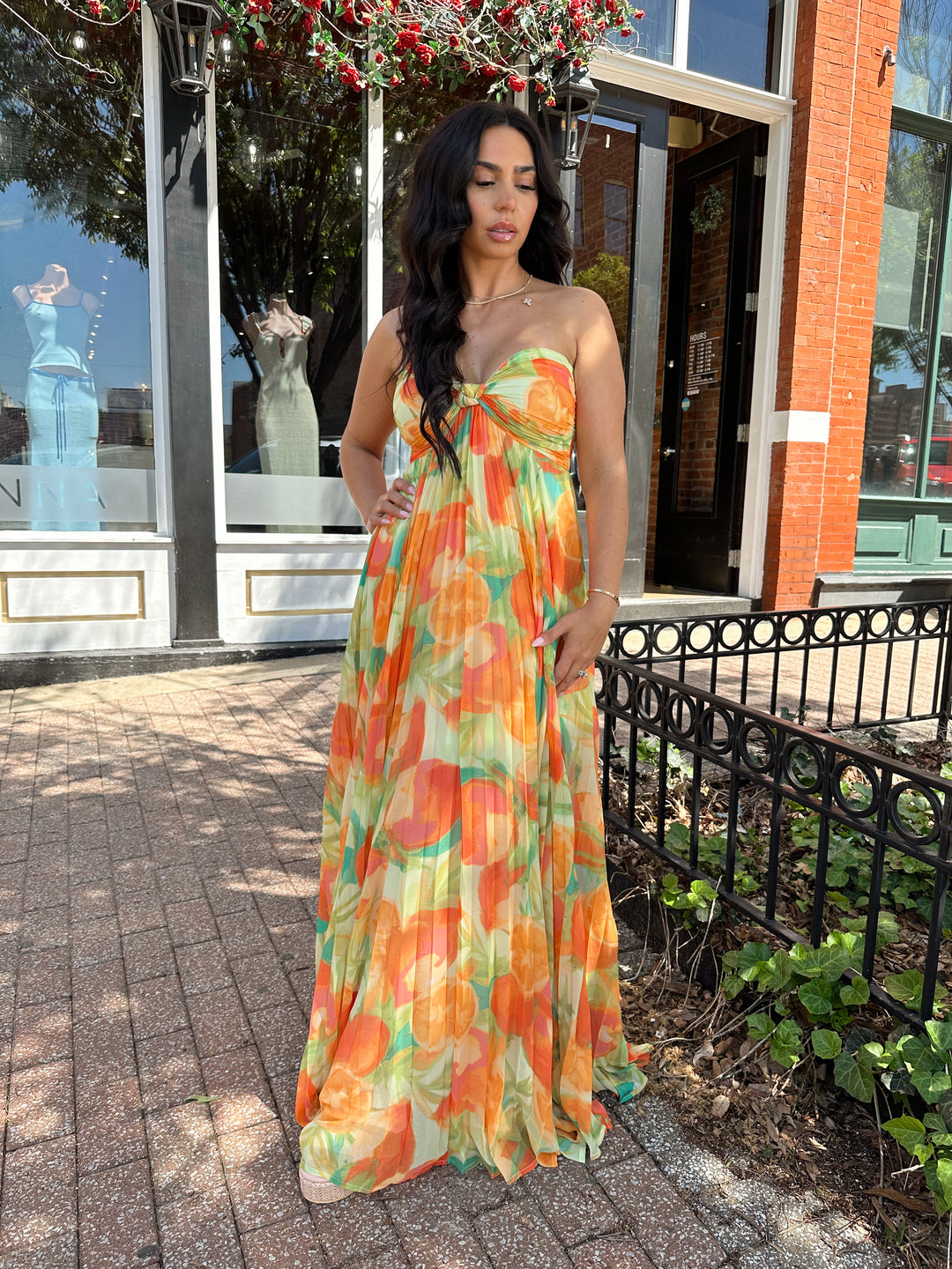 Woman wearing orange tropical plated maxi dress with sweetheart neckline, and knot detail.