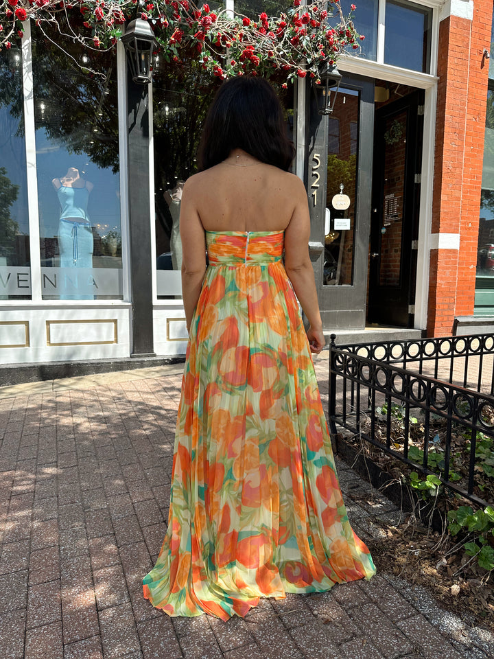 Woman wearing orange tropical plated maxi dress with sweetheart neckline, and knot detail.