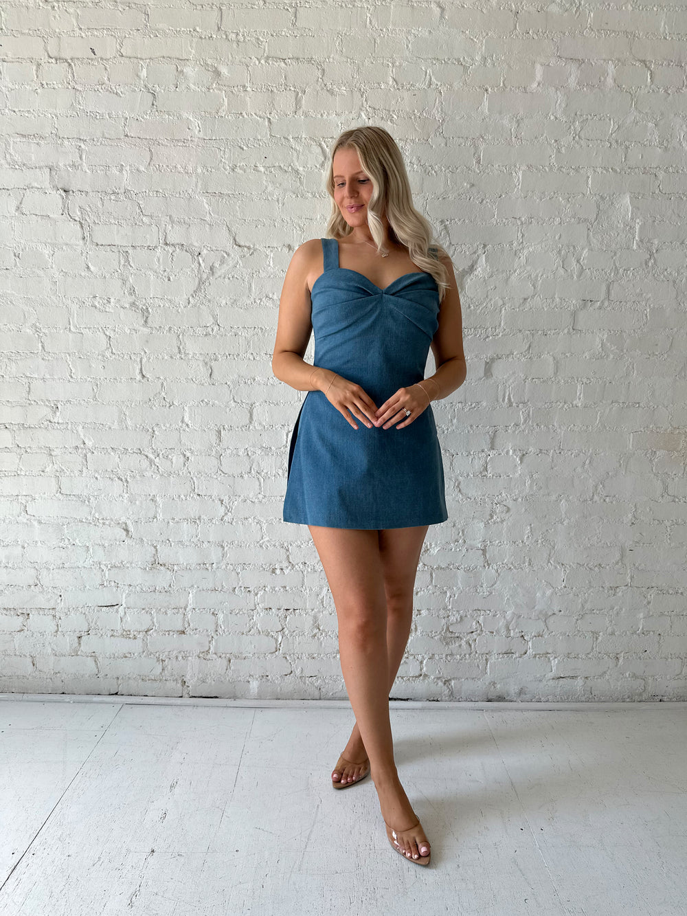 Woman wearing medium wash denim mini dress with built in shorts, and sweetheart neckline. 
