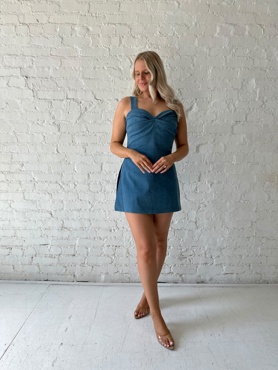 Woman wearing medium wash denim mini dress with built in shorts, and sweetheart neckline. 